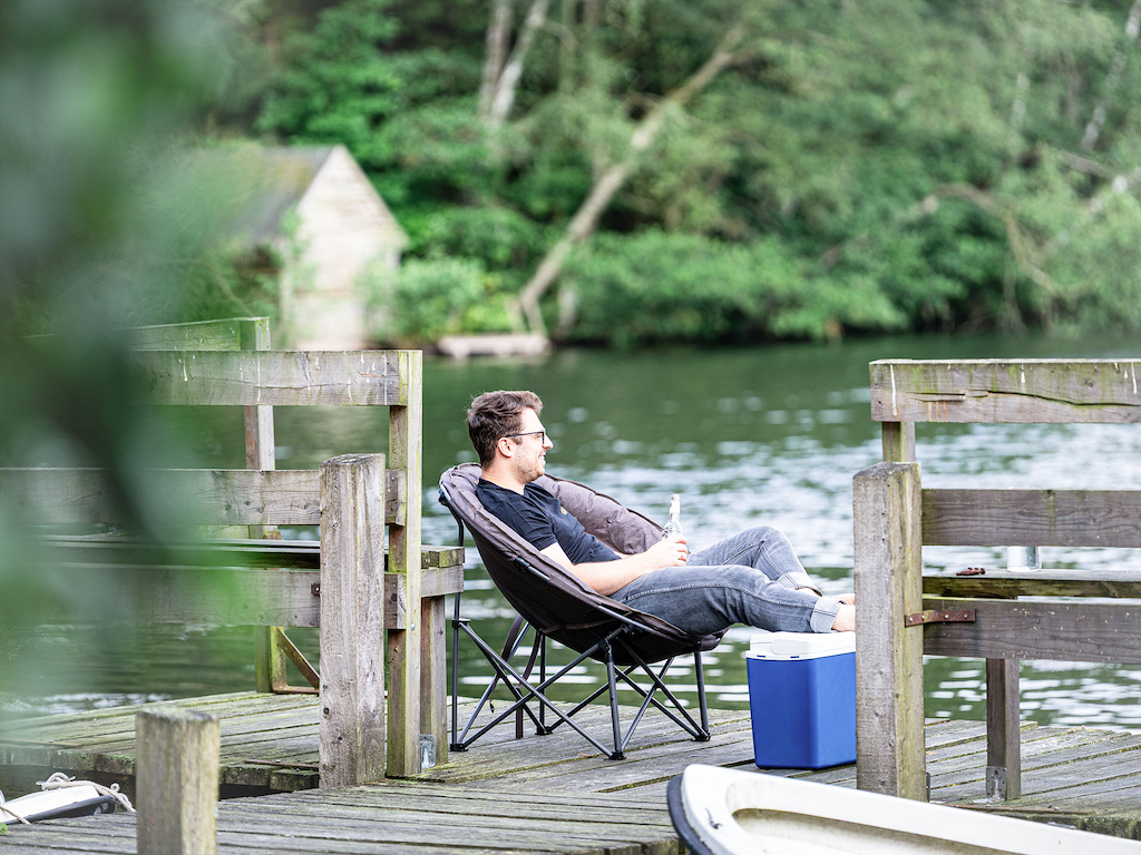 Person sitzt entspannt im uquip CODY Moon Chair auf einem Steg am Wasser